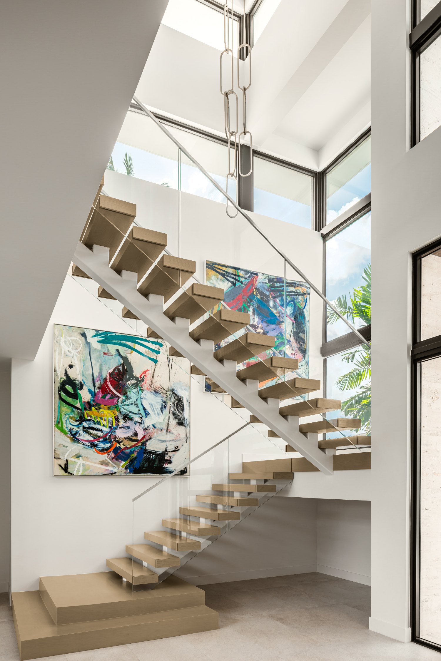 A floating oak staircase climbing past two large abstract paintings beneath clerestory windows