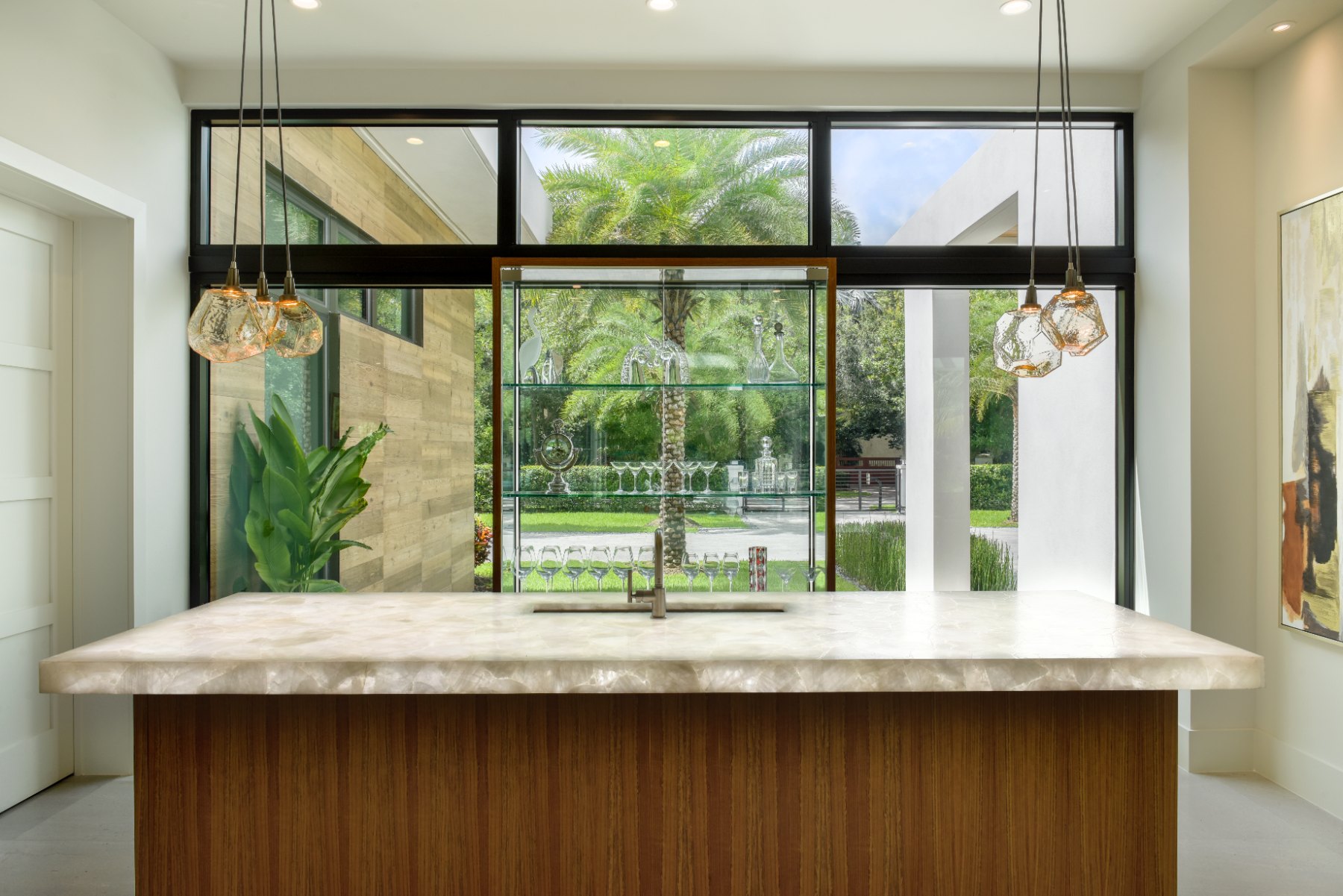 A bar with a glowing stone countertop and walnut base in front of a glass display wall