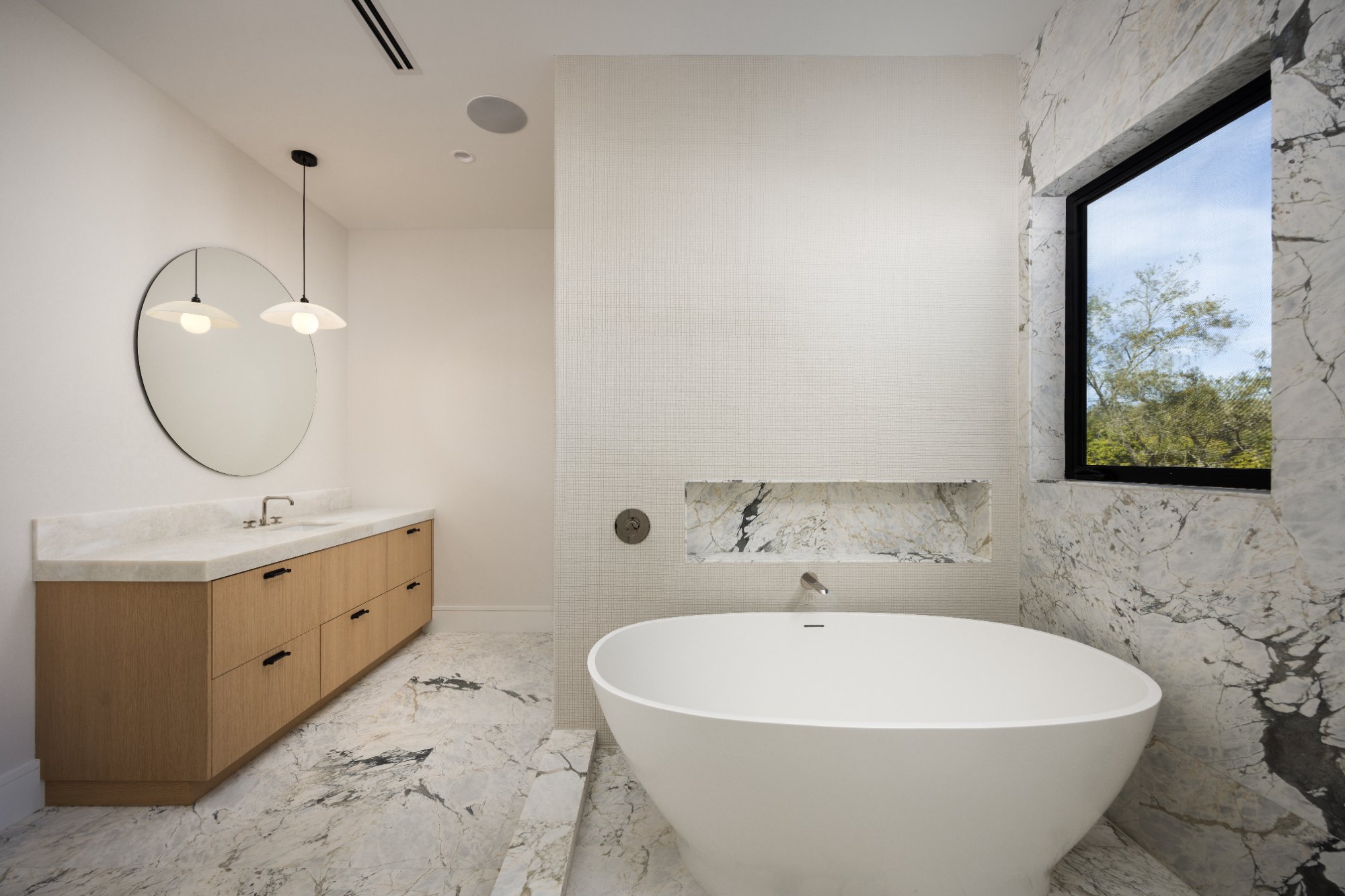 A freestanding tub set against a mosaic wall, with veined stone wrapping the window, floor and niche